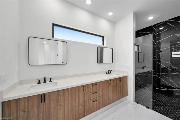 Bathroom with tiled shower, dual bowl vanity, and tile patterned flooring