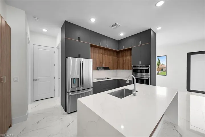 Kitchen featuring sink, light stone counters, an island with sink, light tile patterned floors, and stainless steel appliances