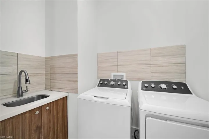 Laundry area featuring sink, independent washer and dryer, and tile walls