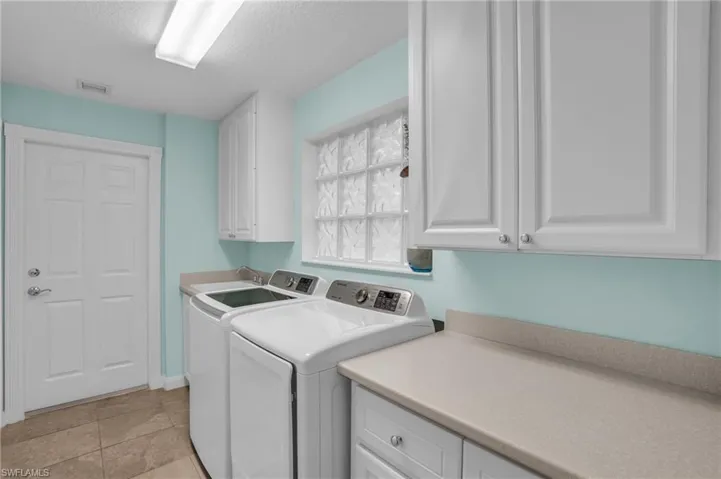 Washroom featuring cabinets, light tile flooring, and washing machine and clothes dryer