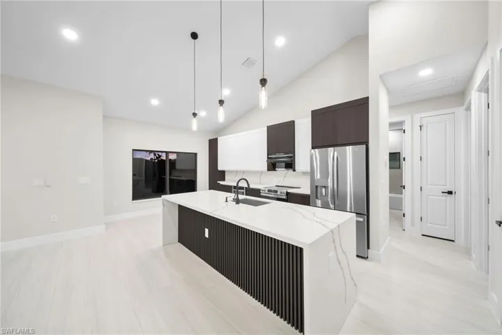 Kitchen featuring pendant lighting, lofted ceiling, stainless steel appliances, modern cabinets, and light stone countertops