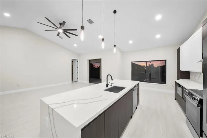 Two tone kitchen with hanging light fixtures, open floor plan, light stone counters, a large island, and stainless steel appliances