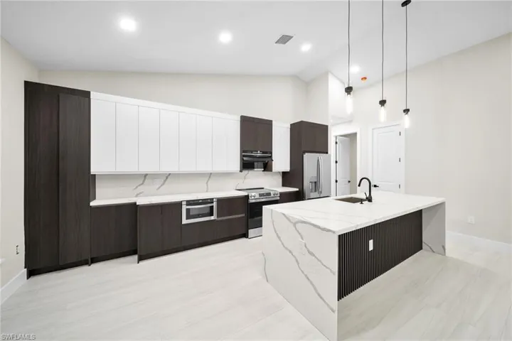 Dual tone kitchen featuring two tone cabinets, modern cabinets, pendant lighting, stainless steel appliances, and lofted ceiling