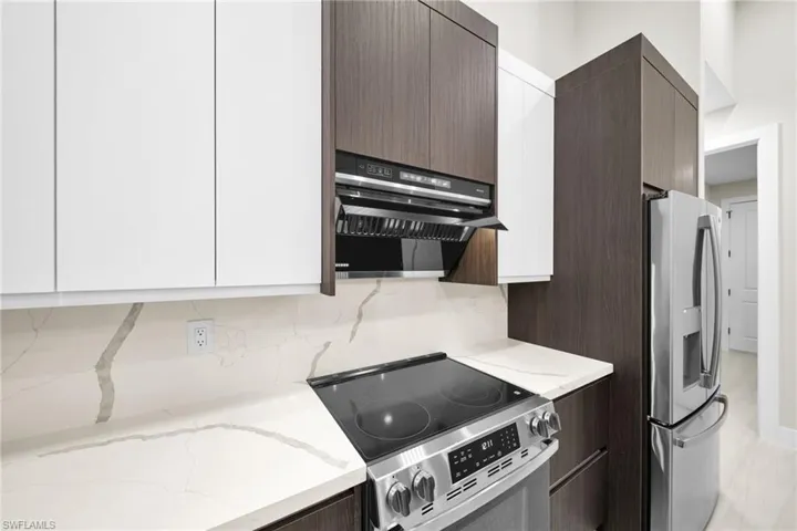 Kitchen with stainless steel appliances, light stone counters, range hood, and modern cabinets