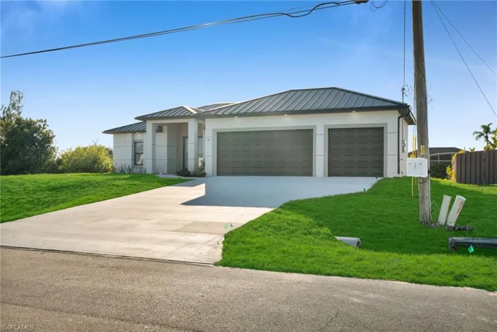View of front of property with a front yard, a standing seam roof, driveway, and a garage
