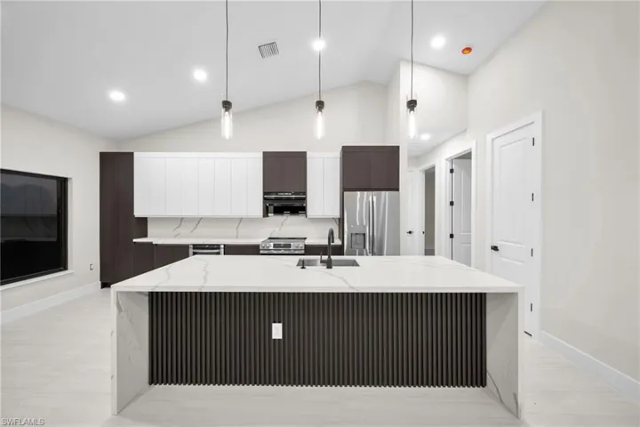 Kitchen with modern cabinets, stainless steel appliances, light stone countertops, a spacious island, and lofted ceiling
