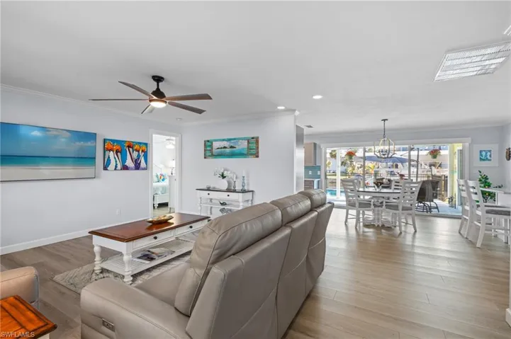 Living room with crown molding, ceiling fan with notable chandelier, and light hardwood / wood-style floors