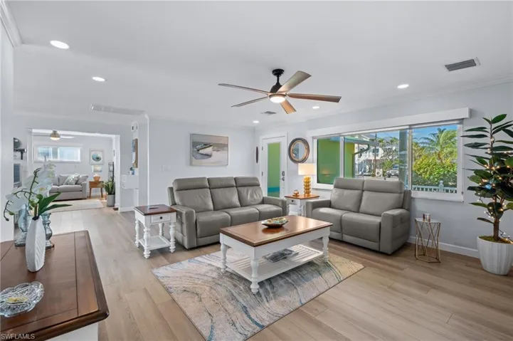 Living room with crown molding, light hardwood / wood-style floors, and ceiling fan, den in background