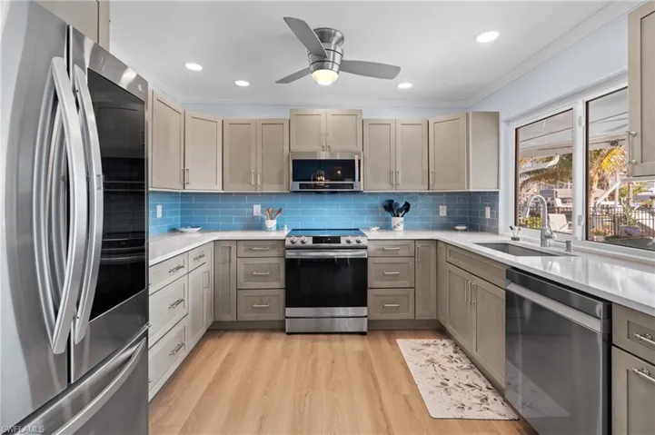 Kitchen with sink, light hardwood / wood-style flooring, ornamental molding, stainless steel appliances, and decorative backsplash