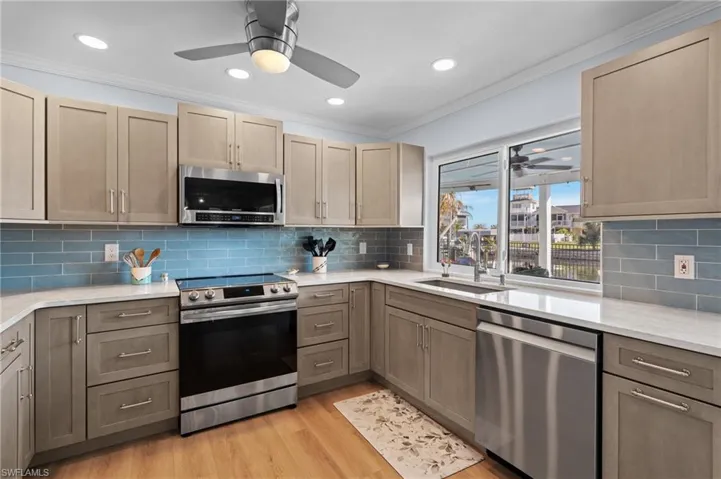 Kitchen featuring sink, crown molding, light wood-type flooring, appliances with stainless steel finishes, and decorative backsplash