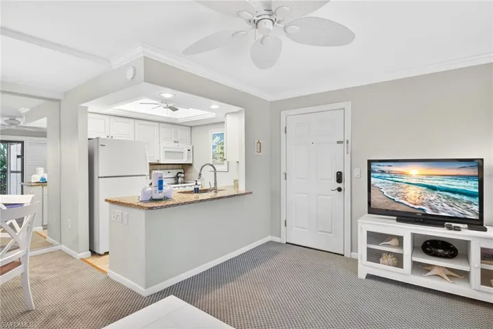 Kitchen featuring white appliances, a peninsula, light carpet, light stone countertops, and crown molding