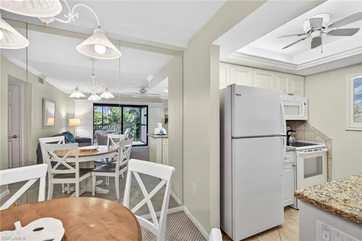 Kitchen featuring a ceiling fan, white appliances, decorative backsplash, a chandelier, and white cabinetry