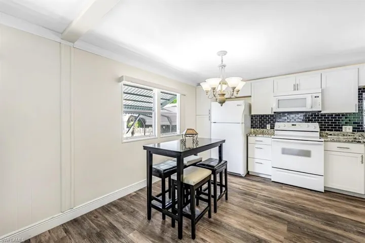 Kitchen with white appliances, light stone countertops, dark hardwood / wood-style flooring, a chandelier, and white cabinetry