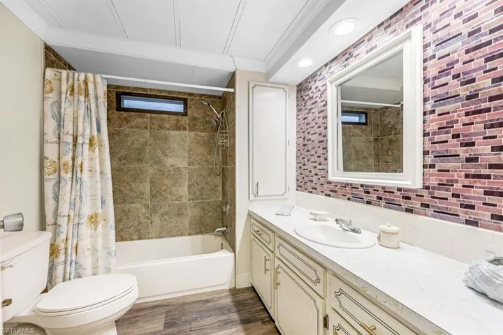 Full bathroom featuring hardwood / wood-style flooring, toilet, shower / tub combo with curtain, vanity, and ornamental molding