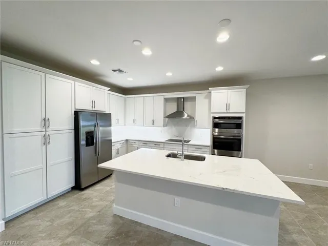Kitchen featuring light stone countertops, white cabinetry, appliances with stainless steel finishes, recessed lighting, and wall chimney exhaust hood