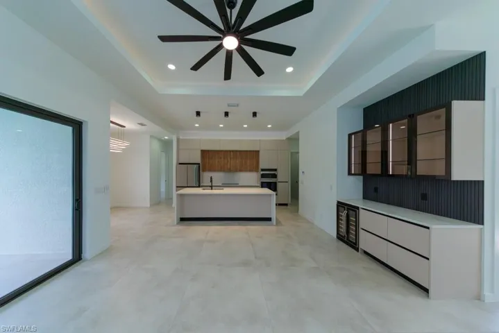 Unfurnished living room featuring a raised ceiling, a ceiling fan, recessed lighting, beverage cooler, and concrete flooring