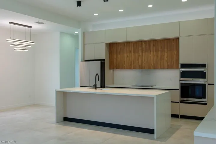 Kitchen with freestanding refrigerator, modern cabinets, stainless steel double oven, light countertops, and an island with sink