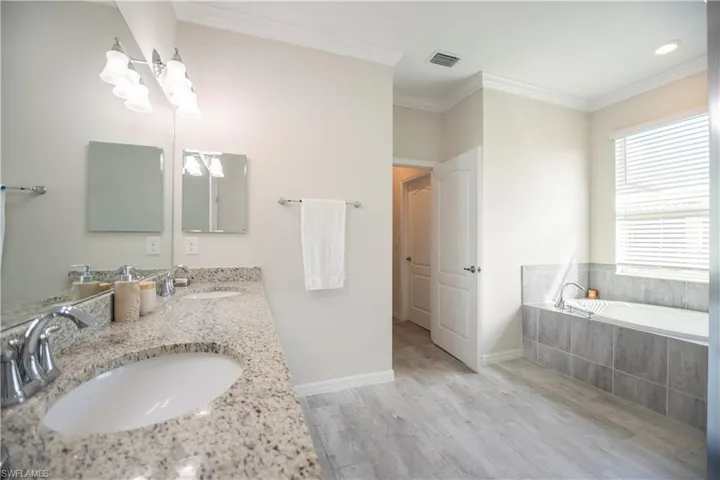 Bathroom with a bath, double vanity, light wood-type flooring, and crown molding