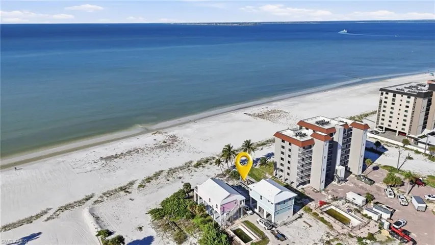 Aerial perspective of beachside property featuring direct shoreline access, elevated structural design, and mature palm trees