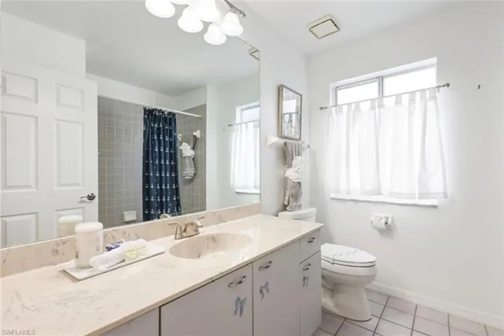 Bathroom with a tile shower, tile patterned floors, toilet, vanity, and baseboards