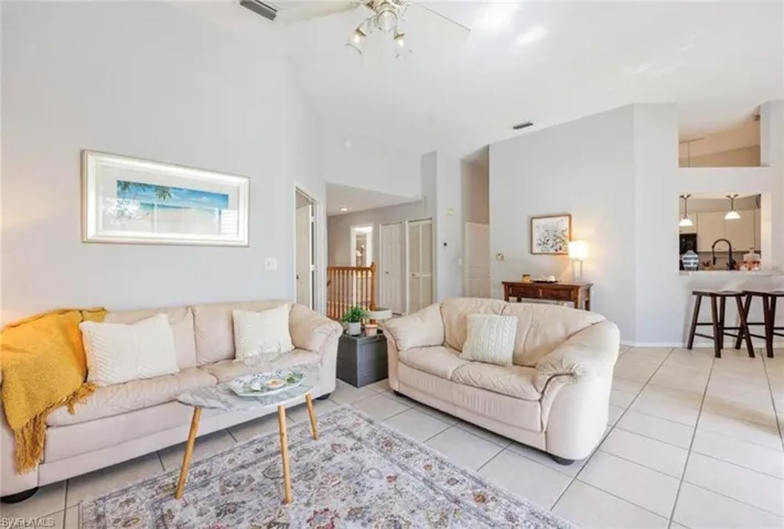 Living room with light tile patterned flooring, baseboards, visible vents, ceiling fan, and high vaulted ceiling