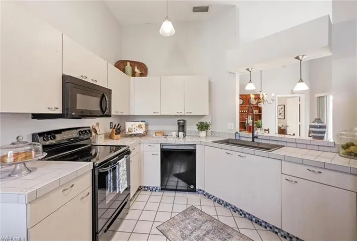 Kitchen featuring tile counters, a sink, black appliances, a towering ceiling, and visible vents
