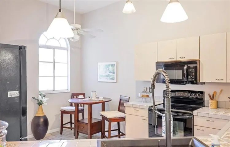 Kitchen with black appliances, a ceiling fan, tile counters, and pendant lighting