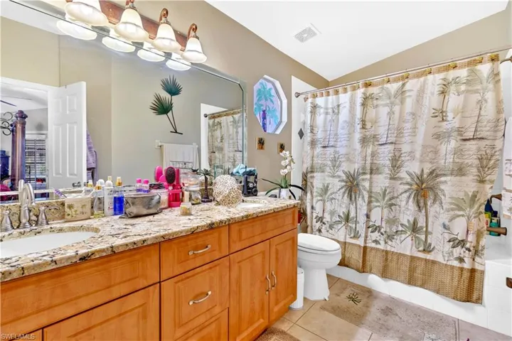 Bathroom with double vanity, shower / bath combination with curtain, light tile patterned floors, and lofted ceiling