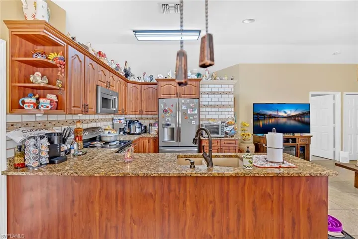 Kitchen with stainless steel appliances, a peninsula, open shelves, light stone counters, and tasteful backsplash