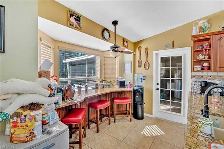 Kitchen with a kitchen breakfast bar, light tile patterned flooring, open shelves, ceiling fan, and light stone countertops