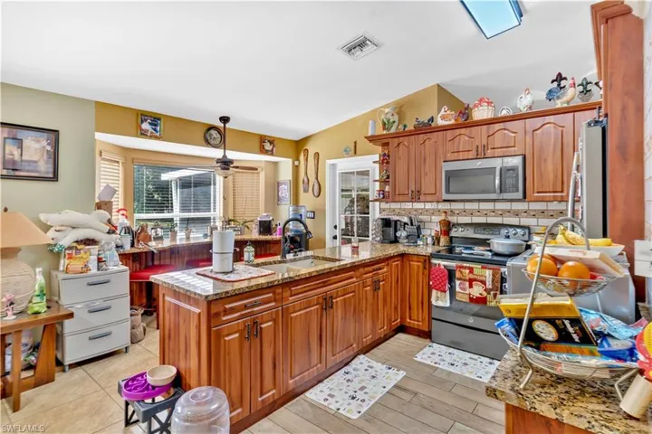 Kitchen featuring wood finish cabinets, stainless steel appliances, a peninsula, light stone countertops, and a ceiling fan