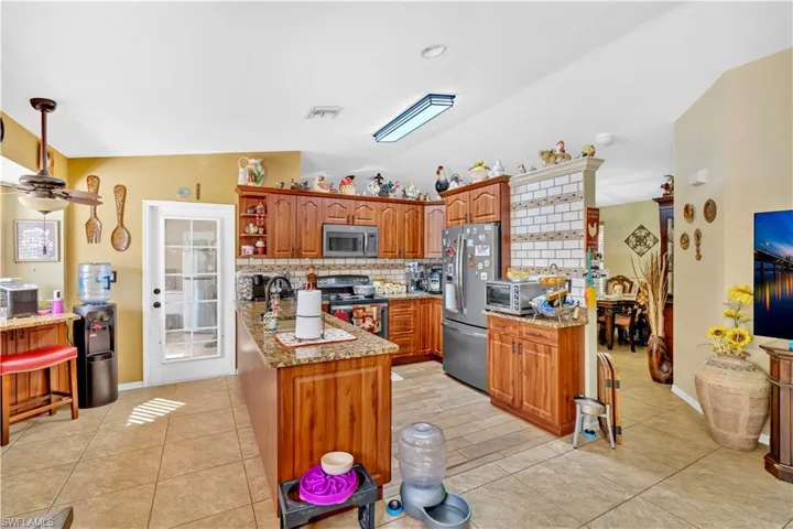 Kitchen with light stone counters, open shelves, stainless steel appliances, wood finish cabinetry, and lofted ceiling