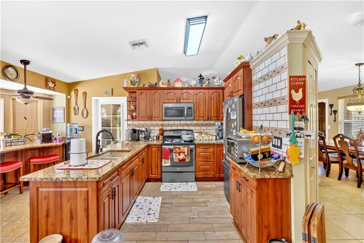 Kitchen featuring decorative light fixtures, stainless steel appliances, a peninsula, wood finish cabinets, and light stone countertops