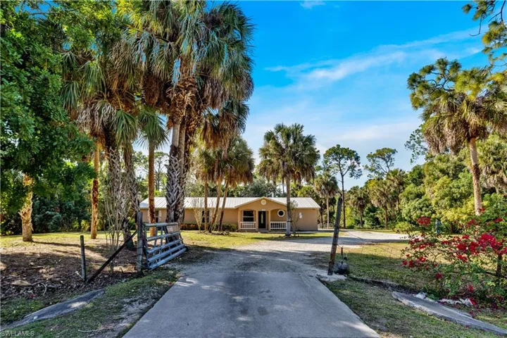 View of front of house with driveway, stucco siding, a metal roof, a front yard, and covered porch