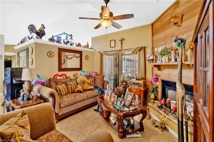 Tiled living room with a glass covered fireplace, ceiling fan, and lofted ceiling