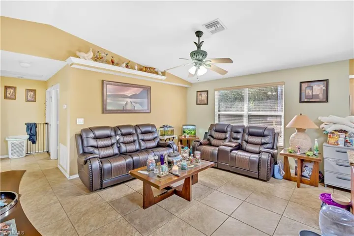 Living room with lofted ceiling, tile patterned flooring, and a ceiling fan