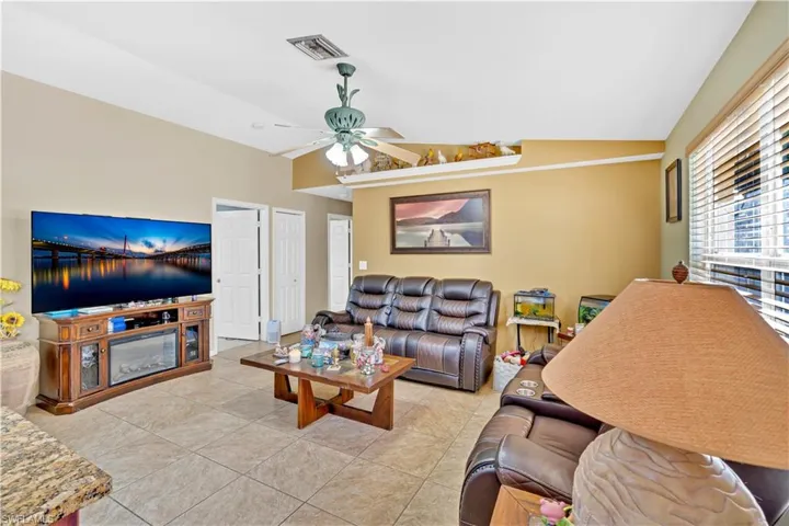 Living area with vaulted ceiling, a ceiling fan, and light tile patterned flooring
