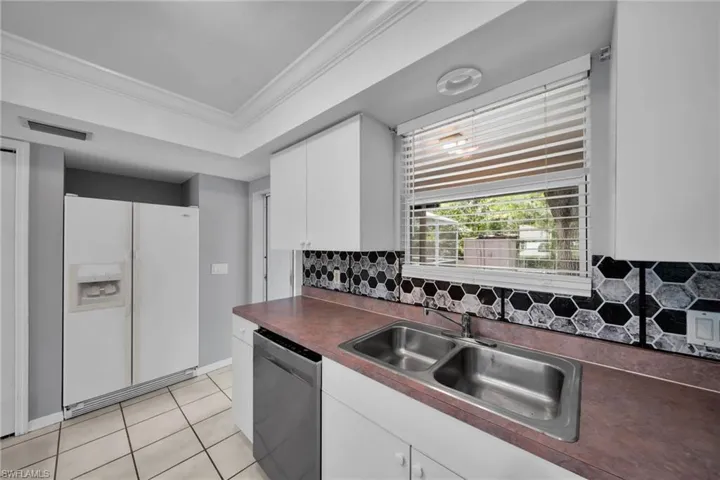 Kitchen featuring white cabinetry, hexagonal tile backsplash, dual basin stainless steel sink, and a large window with horizontal blinds