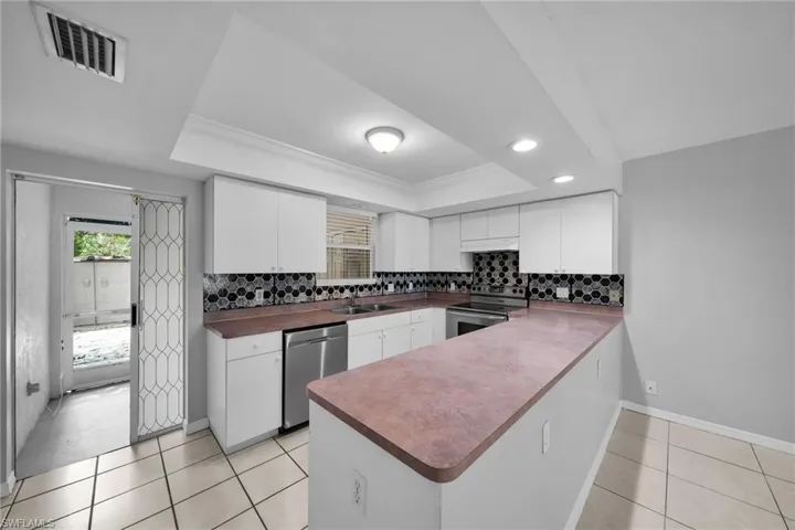 Kitchen featuring white cabinetry, hexagonal tile backsplash, stainless steel appliances, and a pass-through bar with an extended countertop