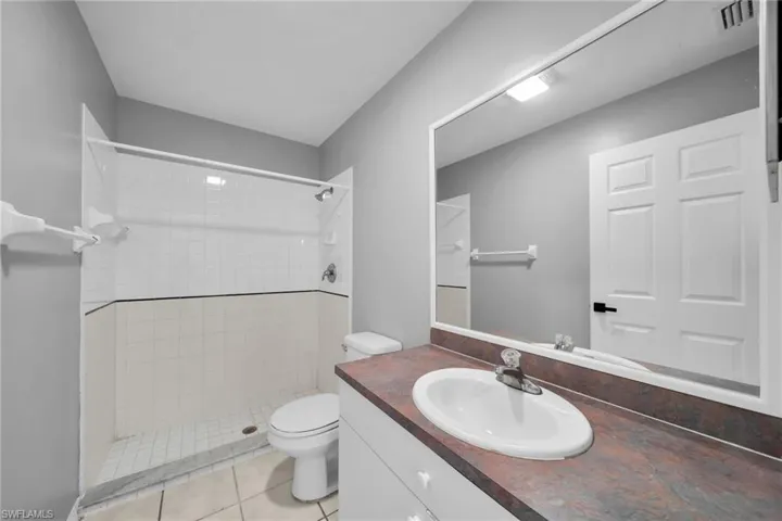 Bathroom featuring a white vanity with an integrated sink, a large wall-mounted mirror, and a shower with white tile surround