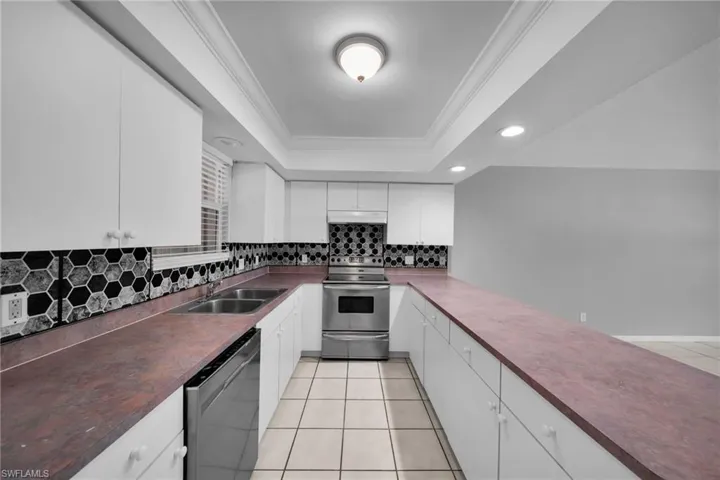 U-shaped kitchen featuring white cabinetry, dark countertops, hexagonal tile backsplash, stainless steel appliances, and recessed lighting