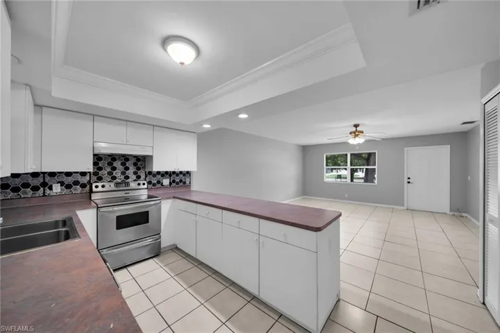 Kitchen featuring white cabinetry, stainless steel range, and a geometric tile backsplash