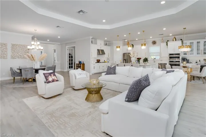 Living room with a chandelier, recessed lighting, light wood-type flooring, crown molding, and a tray ceiling