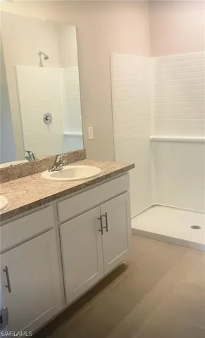 Full bathroom with double vanity, a tile shower, and dark tile patterned flooring