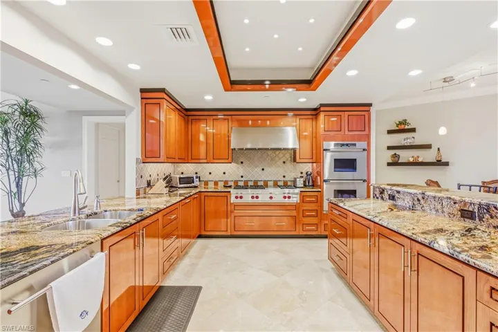 Kitchen with light stone counters, hanging light fixtures, tasteful backsplash, recessed lighting, and stainless steel appliances