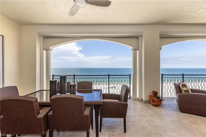 Dining area with a textured ceiling, stone tile floors, a ceiling fan, view of water and beach, and a textured wall