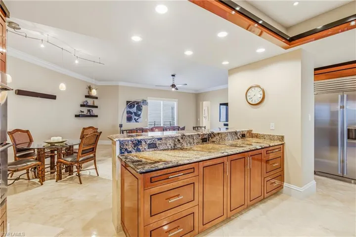 Kitchen with brown cabinets, dark stone counters, recessed lighting, appliances with stainless steel finishes, and ceiling fan