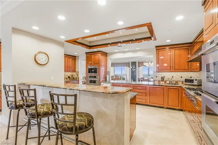Kitchen featuring a breakfast bar area, decorative backsplash, light stone counters, a raised ceiling, and recessed lighting