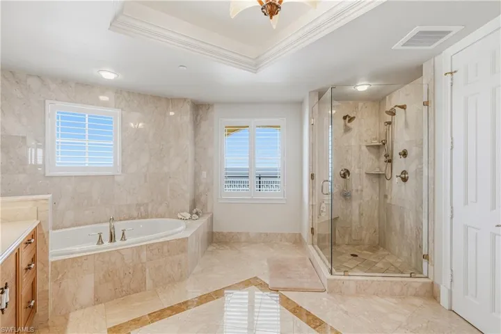 Primary Bathroom featuring plenty of natural light, a tray ceiling, a bath, a stall shower, and ornamental molding