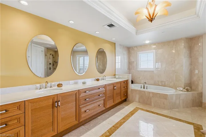 Primary bath with double vanity, a bath, inlaid floor details, a tray ceiling, and recessed lighting